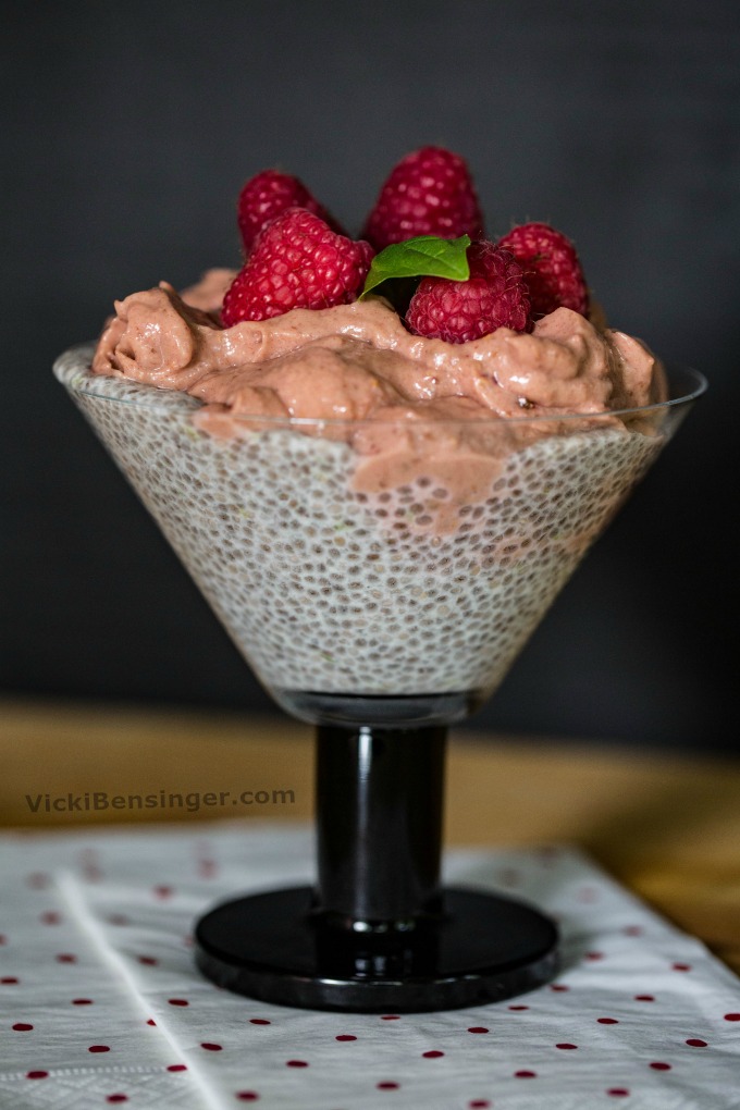 Chia Pudding topped with Raspberry Mousse garnished with fresh Raspberries and a sprig of basil in a parfait glass