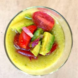 Yellow Gazpacho garnished with avocado, tomatoes, and chopped red onions